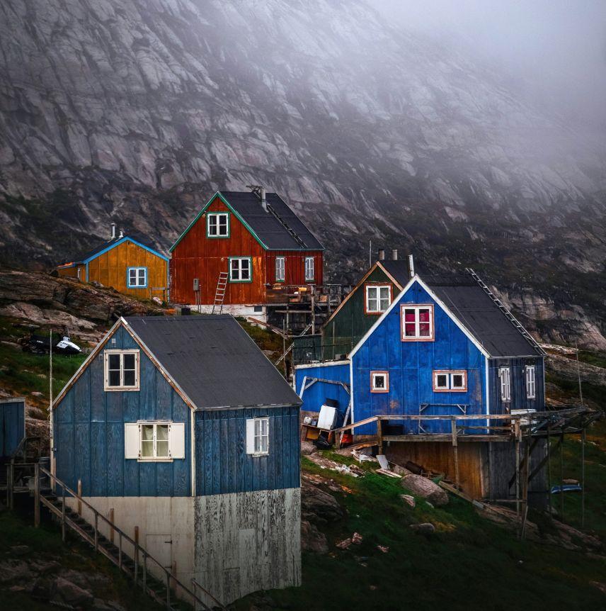 Colorful wooden houses on a green hillside against a misty, dark mountain.